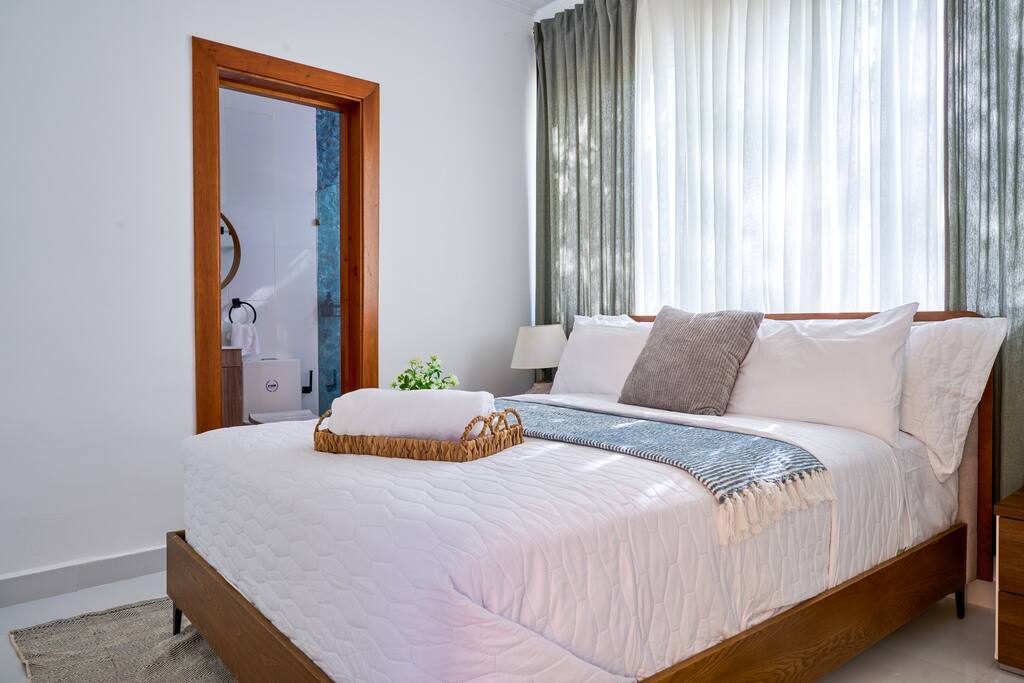 Queen bedroom with soft bedding, bedside tables, and air conditioning for a restful stay.