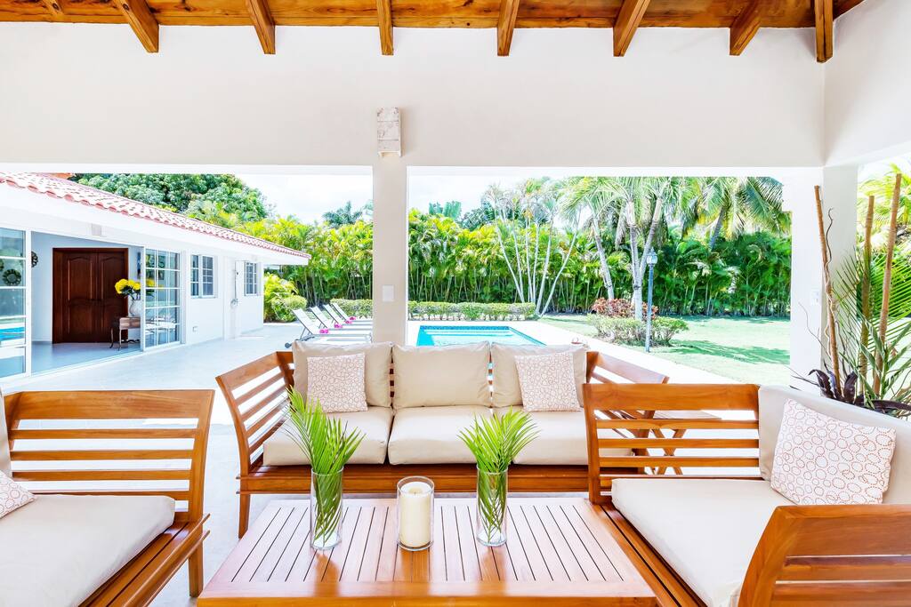 Lovely terrace with cozy sofas just in front of the pool, surrounded by palm trees and other greenery.